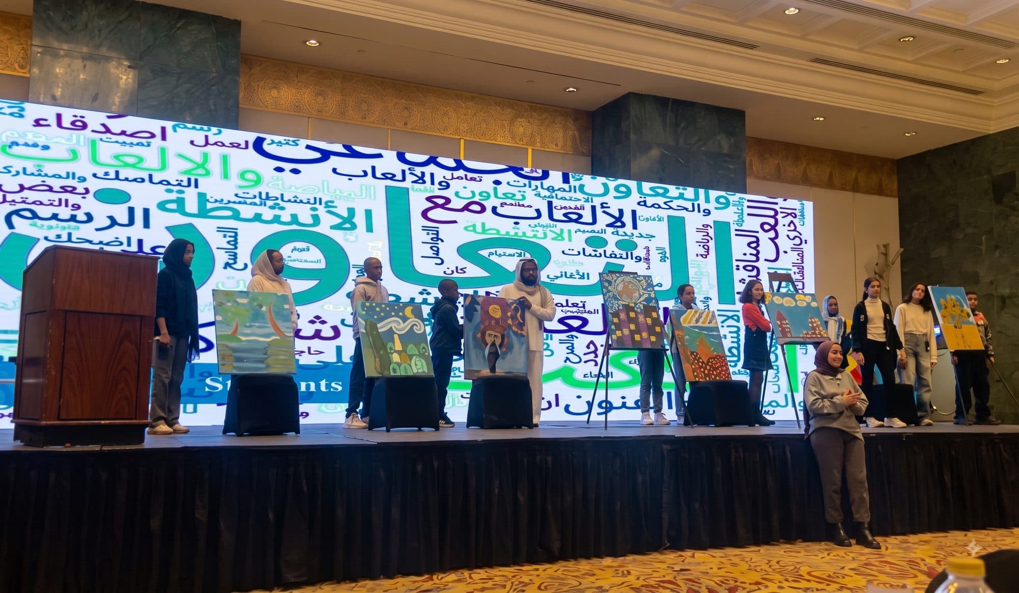 Egyptian and Sudanese students standing on stage holding the paintings they made, in front of a projected wall of words from the program.
